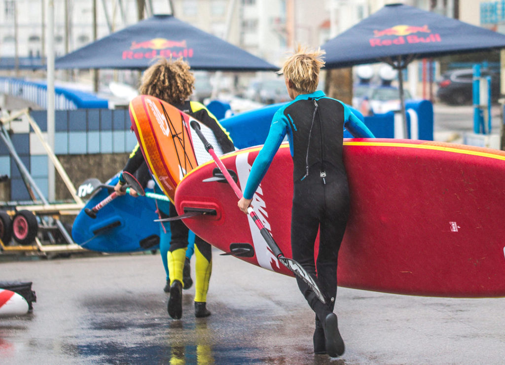 Deux femmes en combinaisons aquatique qui avancent avec leur paddles sous le bras et rame à la main