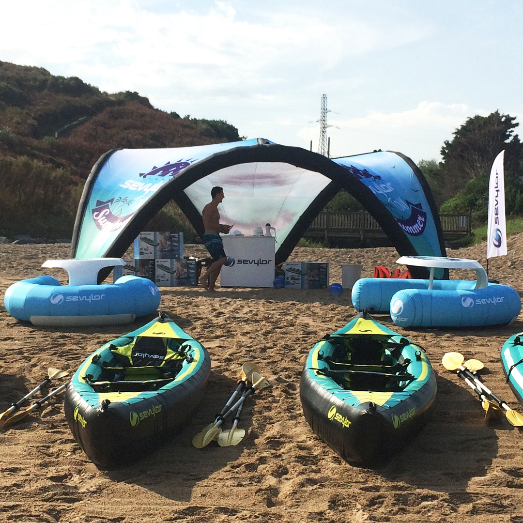 Une plage de sable avec des kayak gonflables alignés au sol et un stand en arrière plan