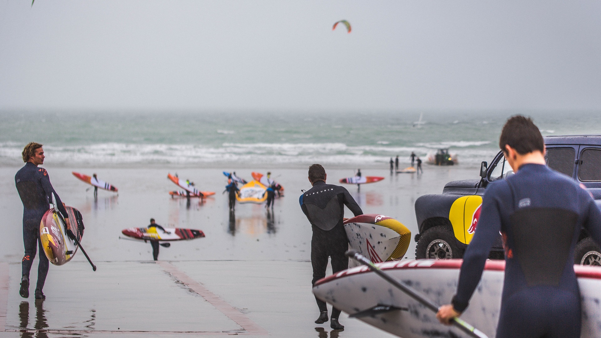 Paul Foulonneau avec son paddle et d'autres personnes sur la plage par mauvais temps