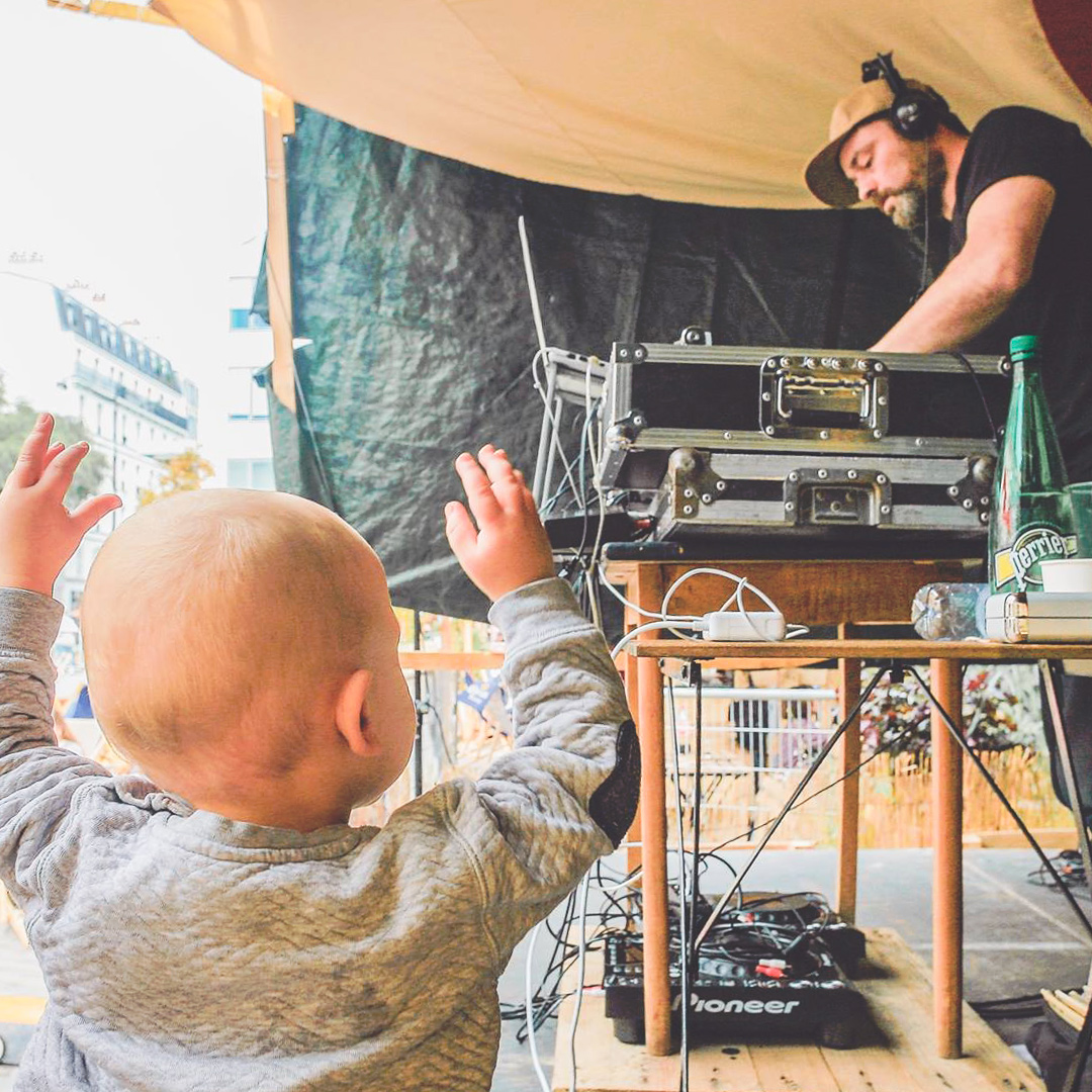 Jeune enfant au premier plan les bras levés devant un DJ sur scène en train de faire de la musique