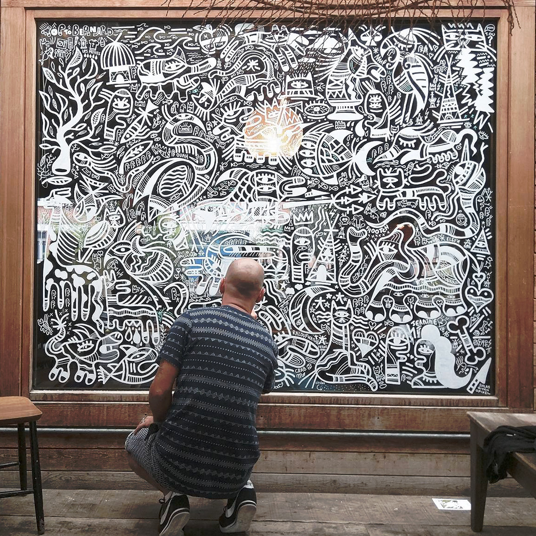 Artiste graffeur en train de peindre un fresque en blanc sur une vitre teintée noire