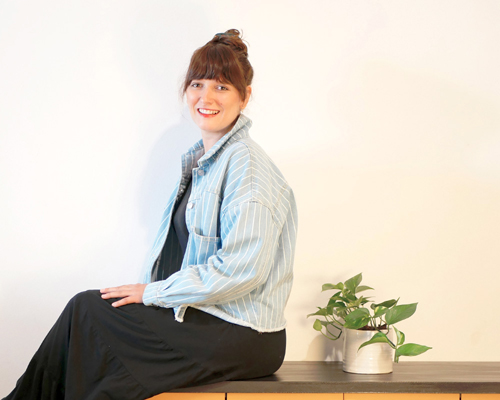 Portrait de Claire notre nouvelle graphiste assise sur un meuble avec une plante verte