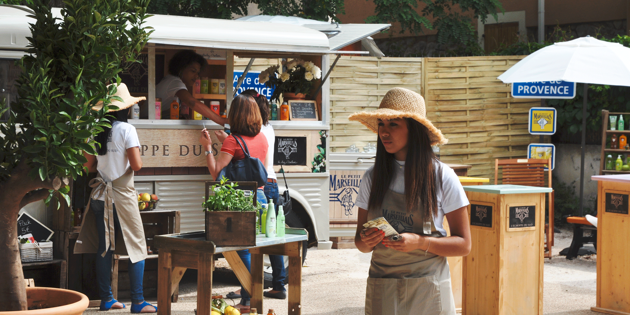 Photographie en plan large de l'espace de présentation des produits petit marseillais avec une présentatrice commerciale au premier plan