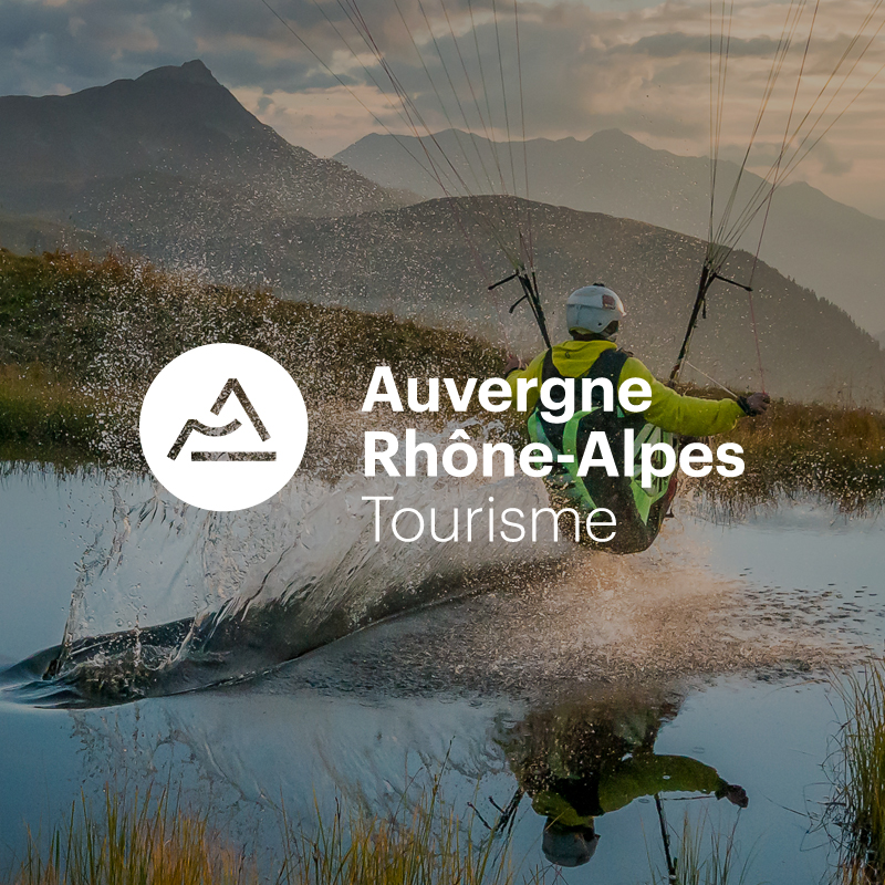 Homme en deltaplane sur un lac avec logo Aura Tourisme en blanc