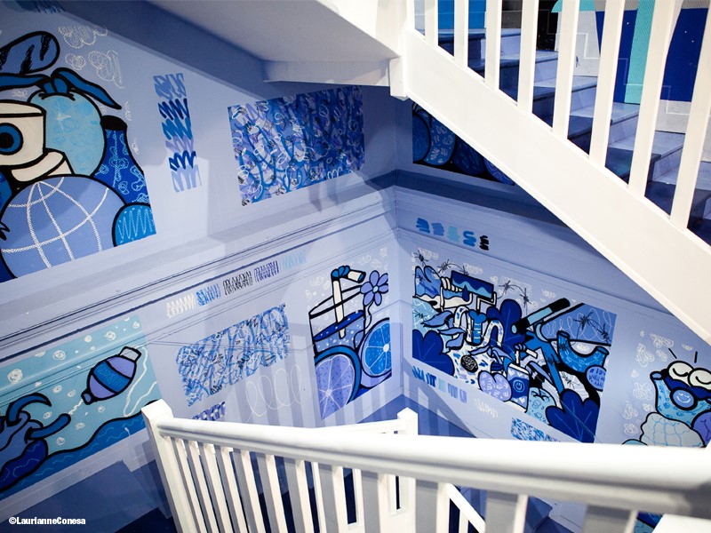 Cage d'escalier de l'hotel colorama de Biarritz avec des dessins bleu de gobelet, d'eau et des oeuvres abstraites sur les murs autour d'une rampe d'escalier blanche immaculée