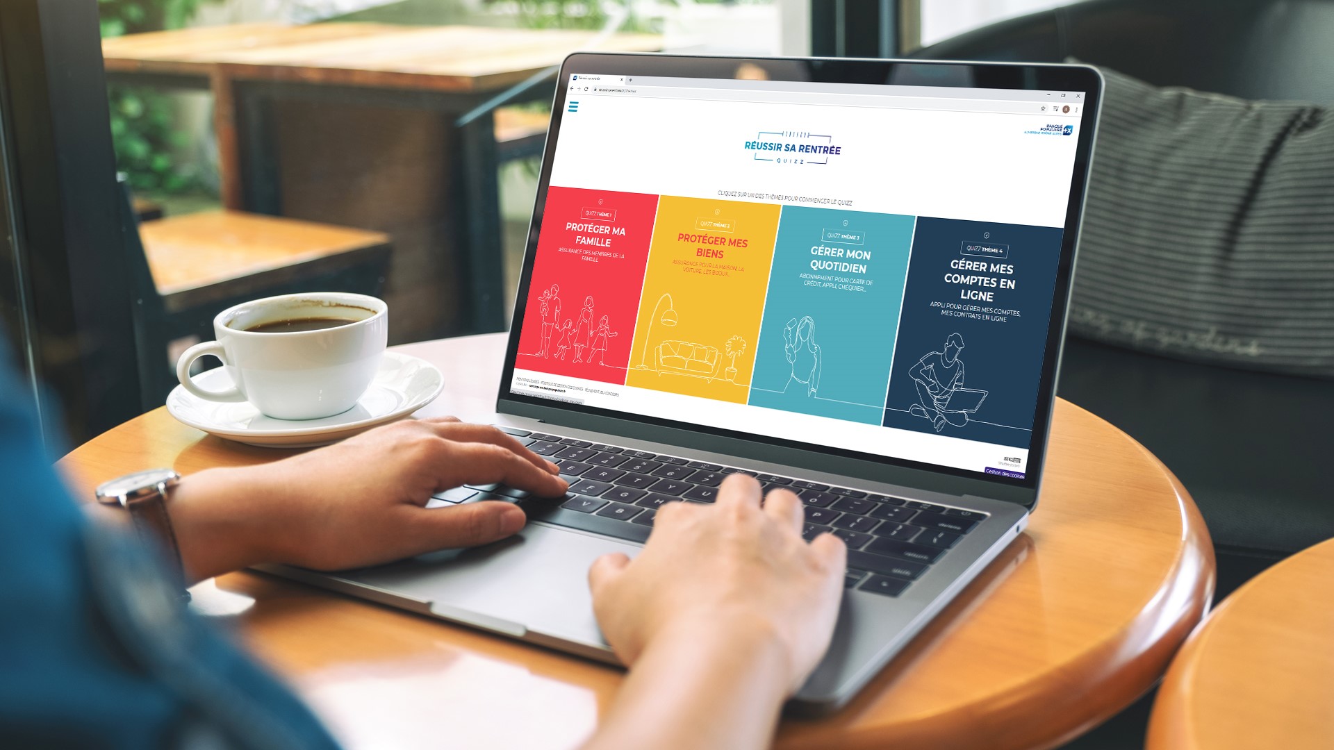 Personne dans un café avec le mains posées sur le clavier d'un ordinateur portable ouvert sur le site internet de Banque Populaire